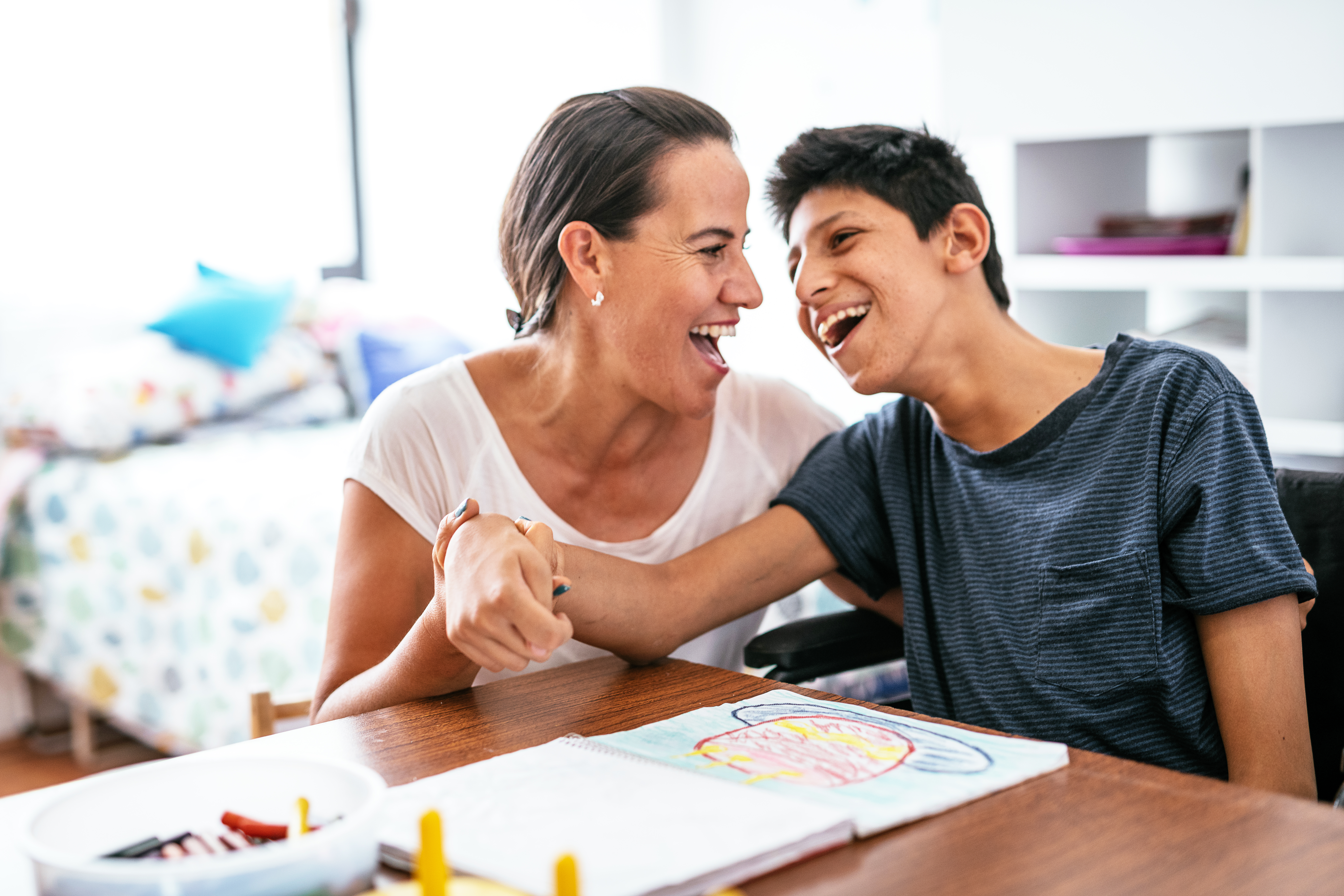 Young participant living with Cerebral Palsy is connecting and laughing with his mother, whilst engaging in drawing activities.